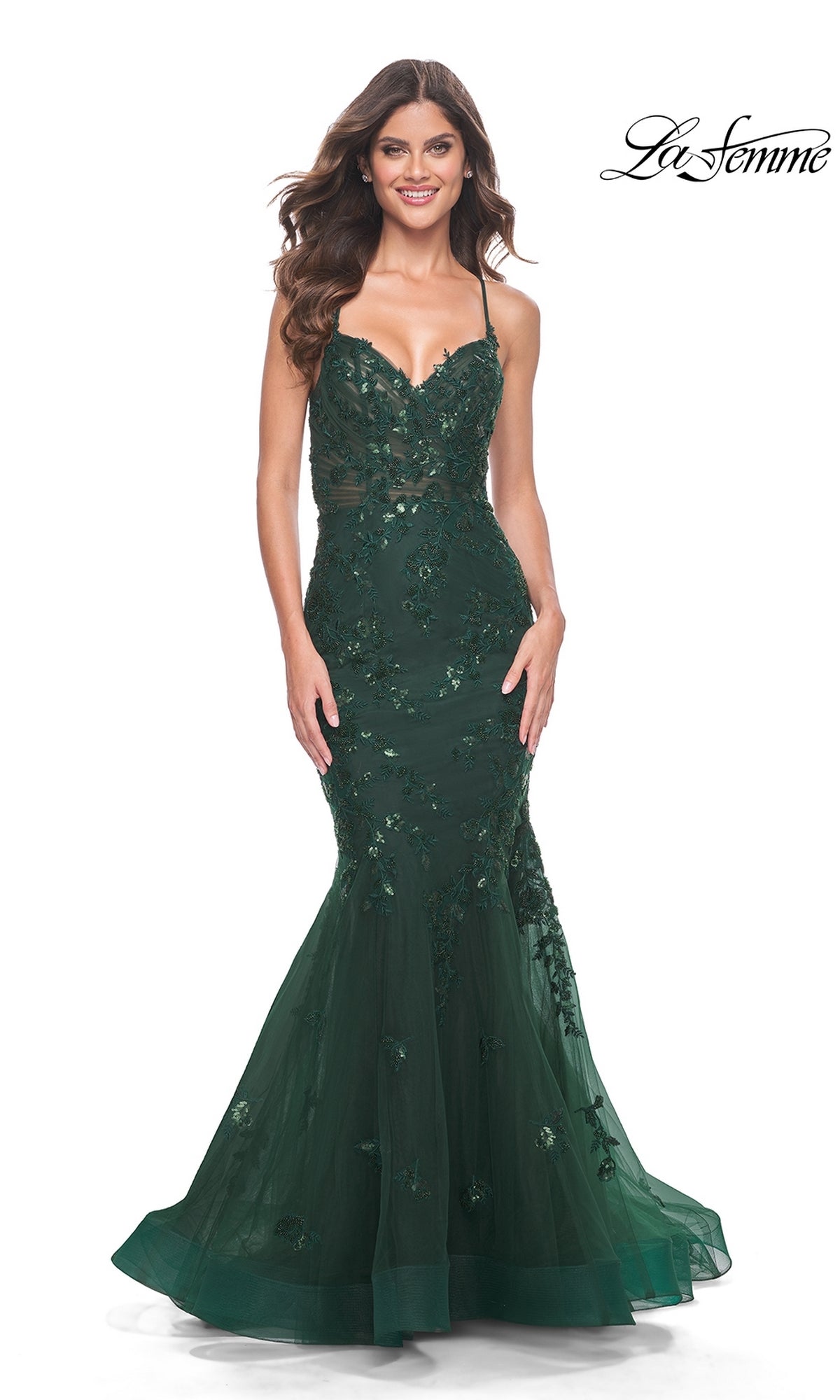 A woman in the La Femme Tonal Lace Long Mermaid Prom Dress 32033, featuring dark green strapless fitted design, beaded lace, and floral embellishments, stands smiling. The